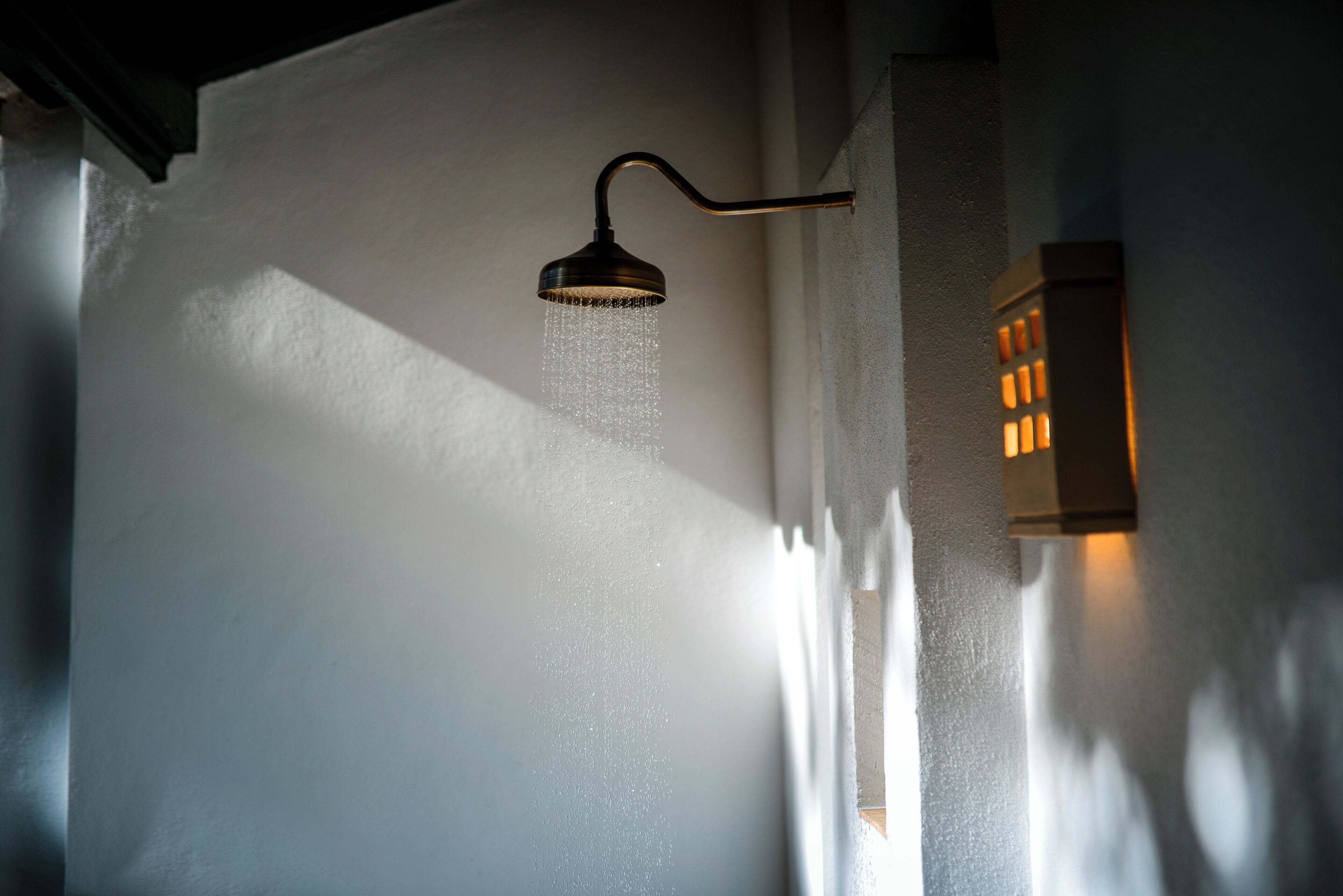 A showerhead with water flowing, mounted on a wall with a light fixture beside it.