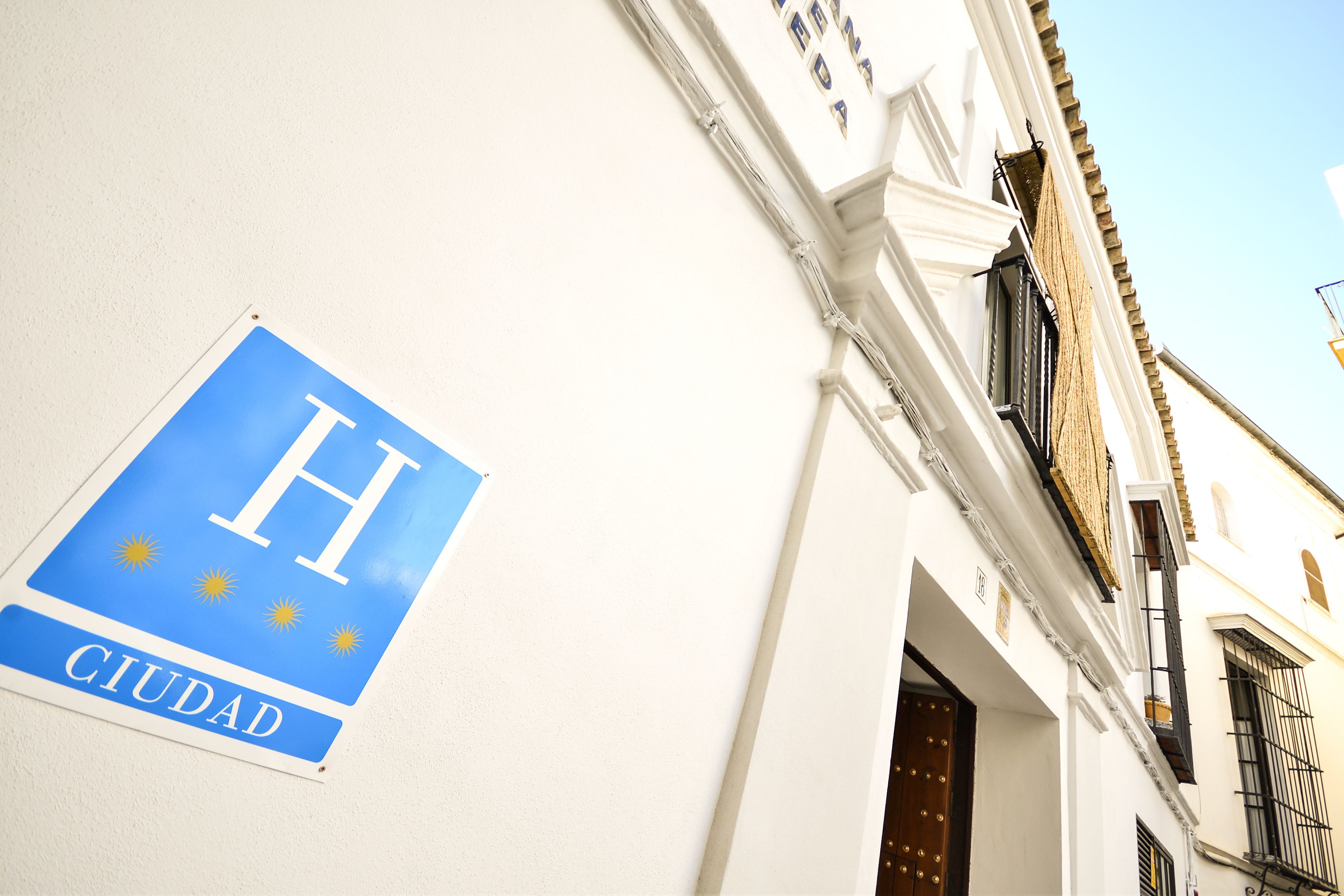 A sign with a blue background and white letters spelling "H CIUDAD" on a white wall.