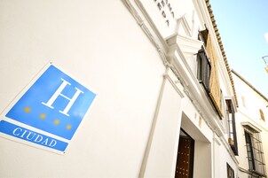 A sign with a blue background and white letters spelling "H CIUDAD" on a white wall.