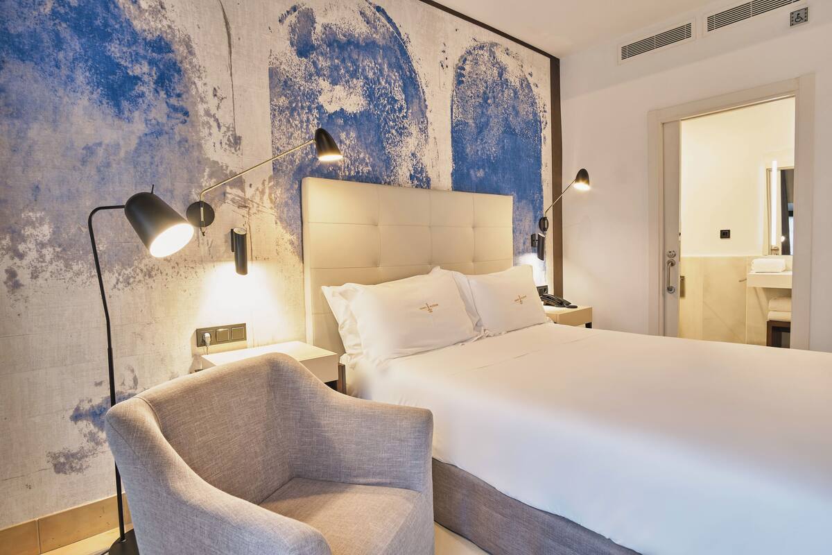 A hotel room with a large bed, a chair, and a wall with a textured design.