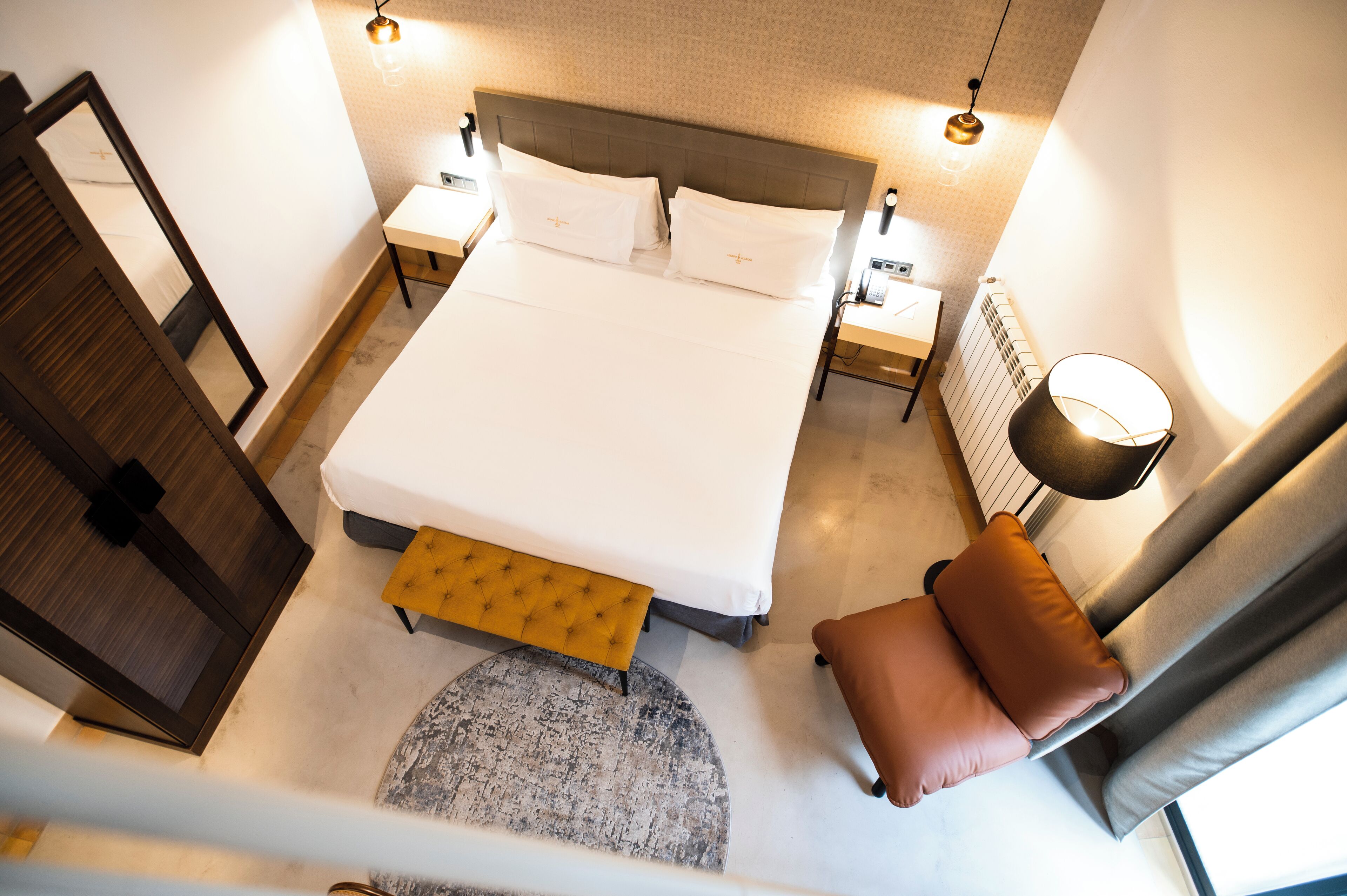 A bedroom with a bed, bedside tables, a nightstand, a lamp, a bench, and a window with curtains.
