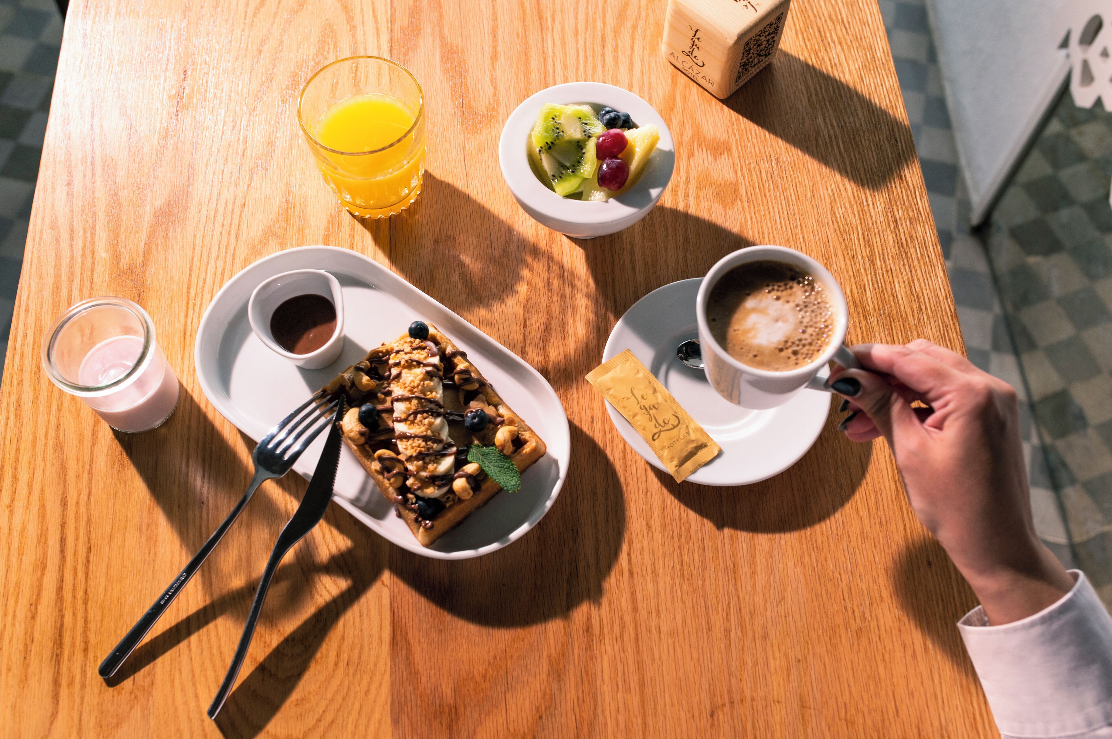 Un desayuno con un gofre, café y fruta sobre una mesa de madera.