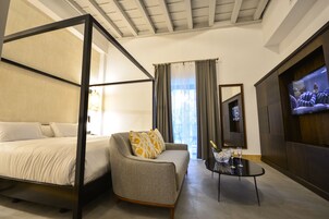 A hotel room with a four-poster bed, a sofa, a TV, and a small table with a bottle and glasses.