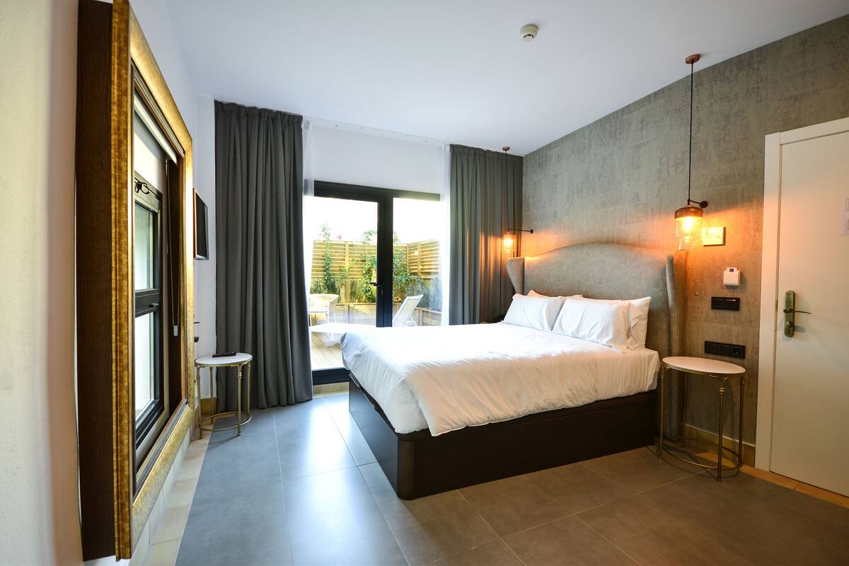 A modern hotel room with a large bed, a small round table, and a view of the outdoor area.