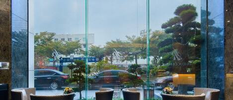 A modern lobby with a glass wall, seating area with wicker chairs, and a polished marble floor.
