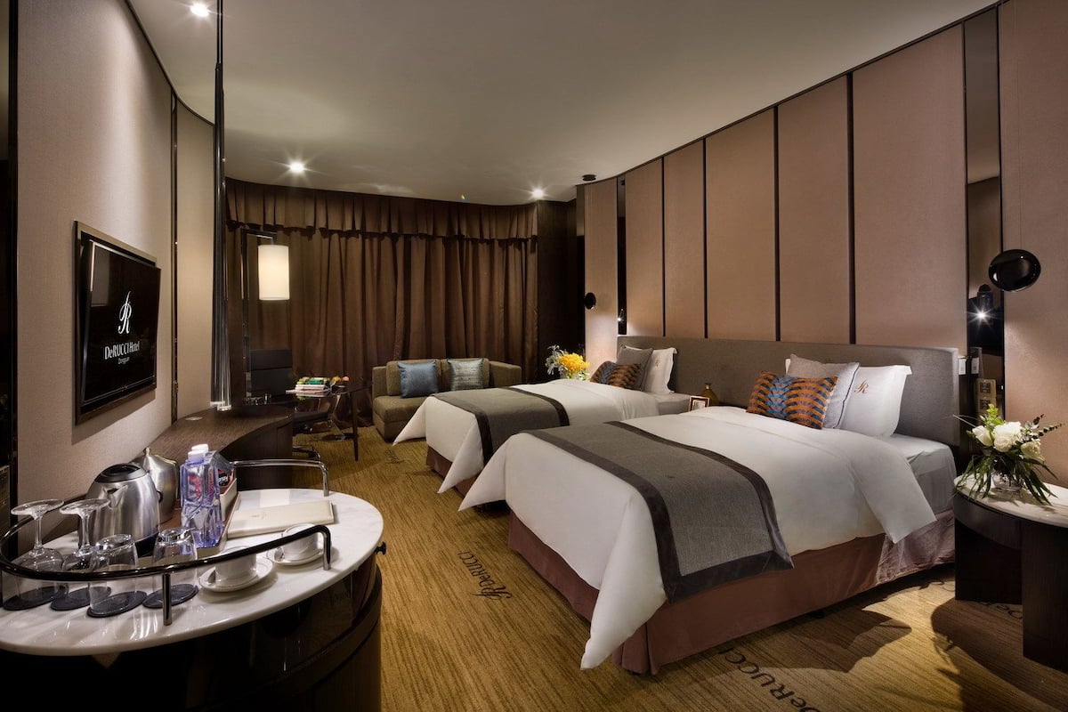 A hotel room with two beds, a desk with a chair, a television, and a minibar.