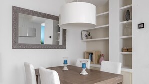 Ein Essbereich mit einem Holztisch, weißen Stühlen, einem großen Spiegel und einer Pendelleuchte.