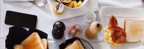 Une table mise pour le petit-déjeuner avec des toasts, des œufs brouillés, du bacon et un bol de fruits.