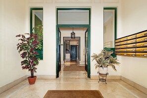Un couloir avec une porte à cadre vert, une plante en pot et un classeur fixé au mur.