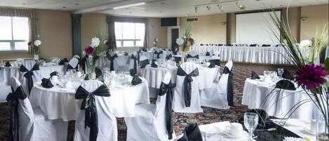 A banquet hall with round tables, white tablecloths, and black sashes.