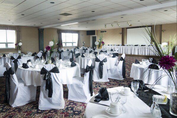 Un salón de banquetes con mesas redondas, manteles blancos y cintas negras.
