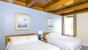 Habitación de hotel con dos camas, techo de madera y cuadros enmarcados en la pared.