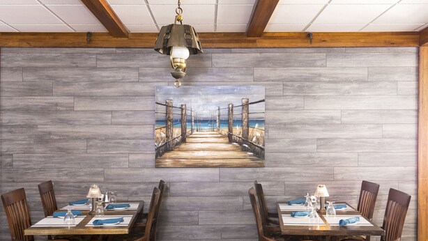 Un comedor con una mesa y sillas de madera, un cuadro de un muelle y una lámpara colgante.
