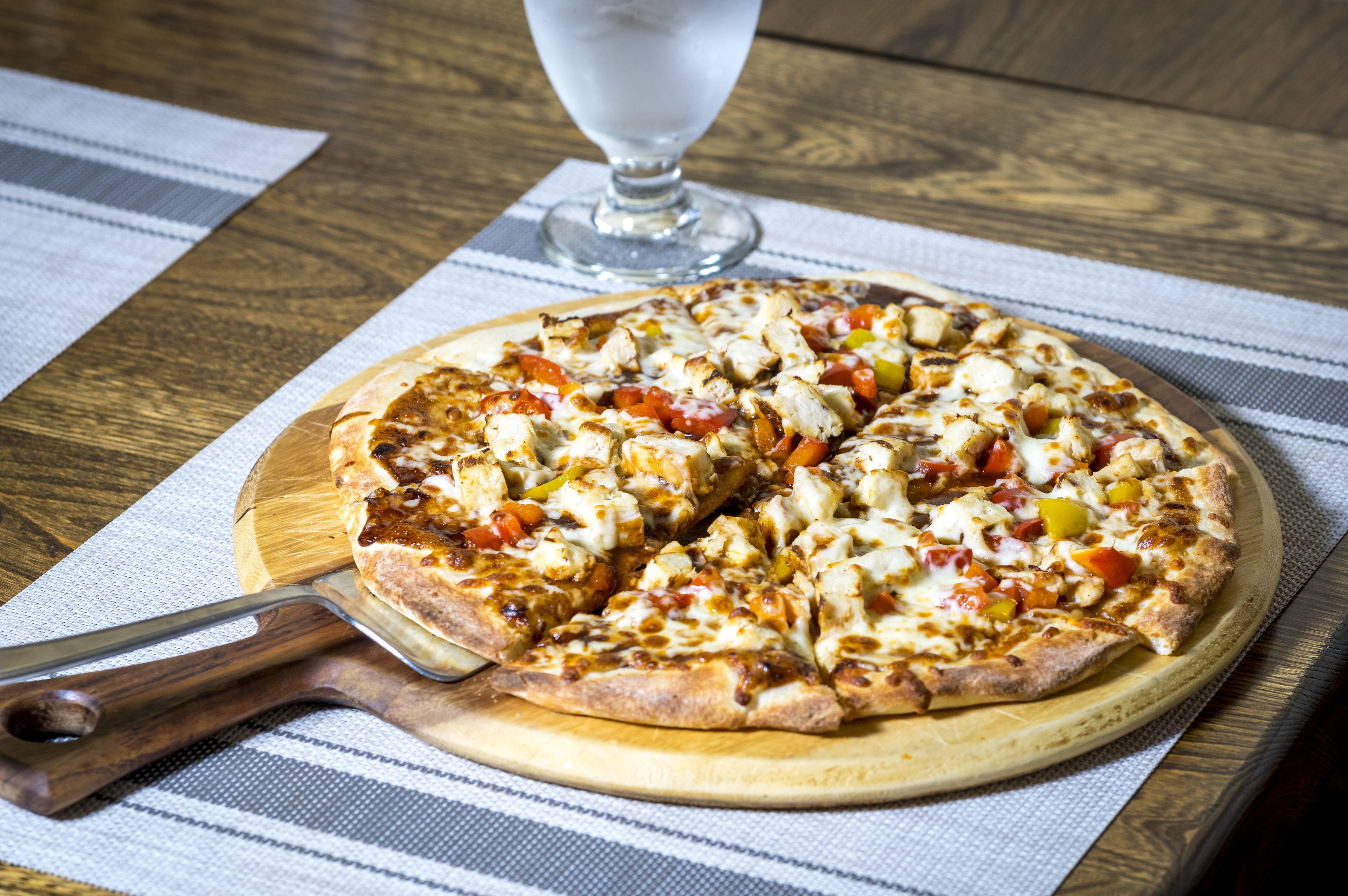 Eine Pizza auf einem Holzboden mit einem Pizzaschneider daneben, auf einem gestreiften Tuch platziert.