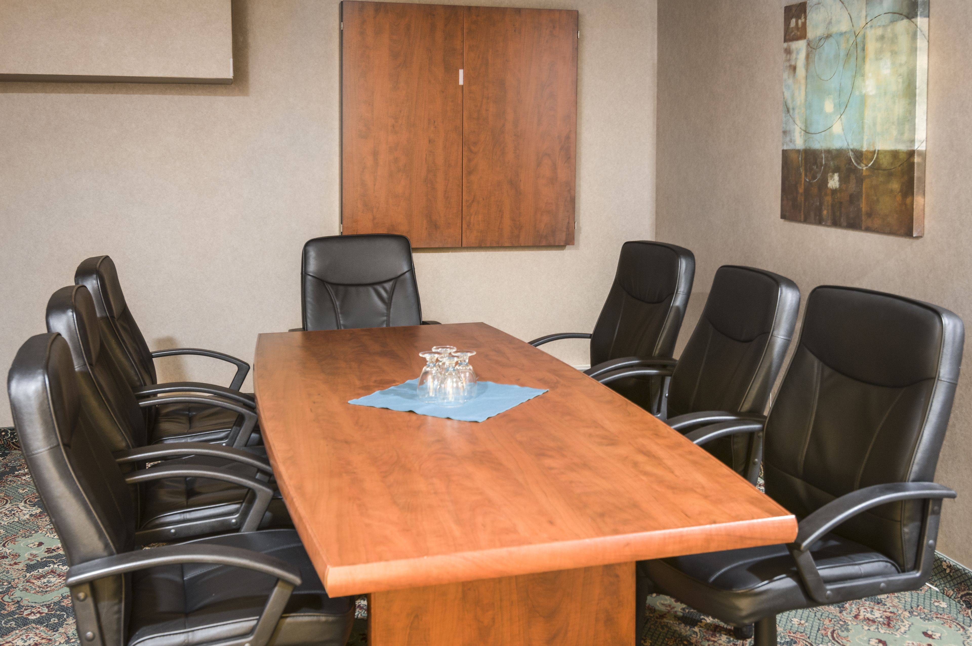 A conference room with a wooden table, six black leather chairs, and a blue placemat.