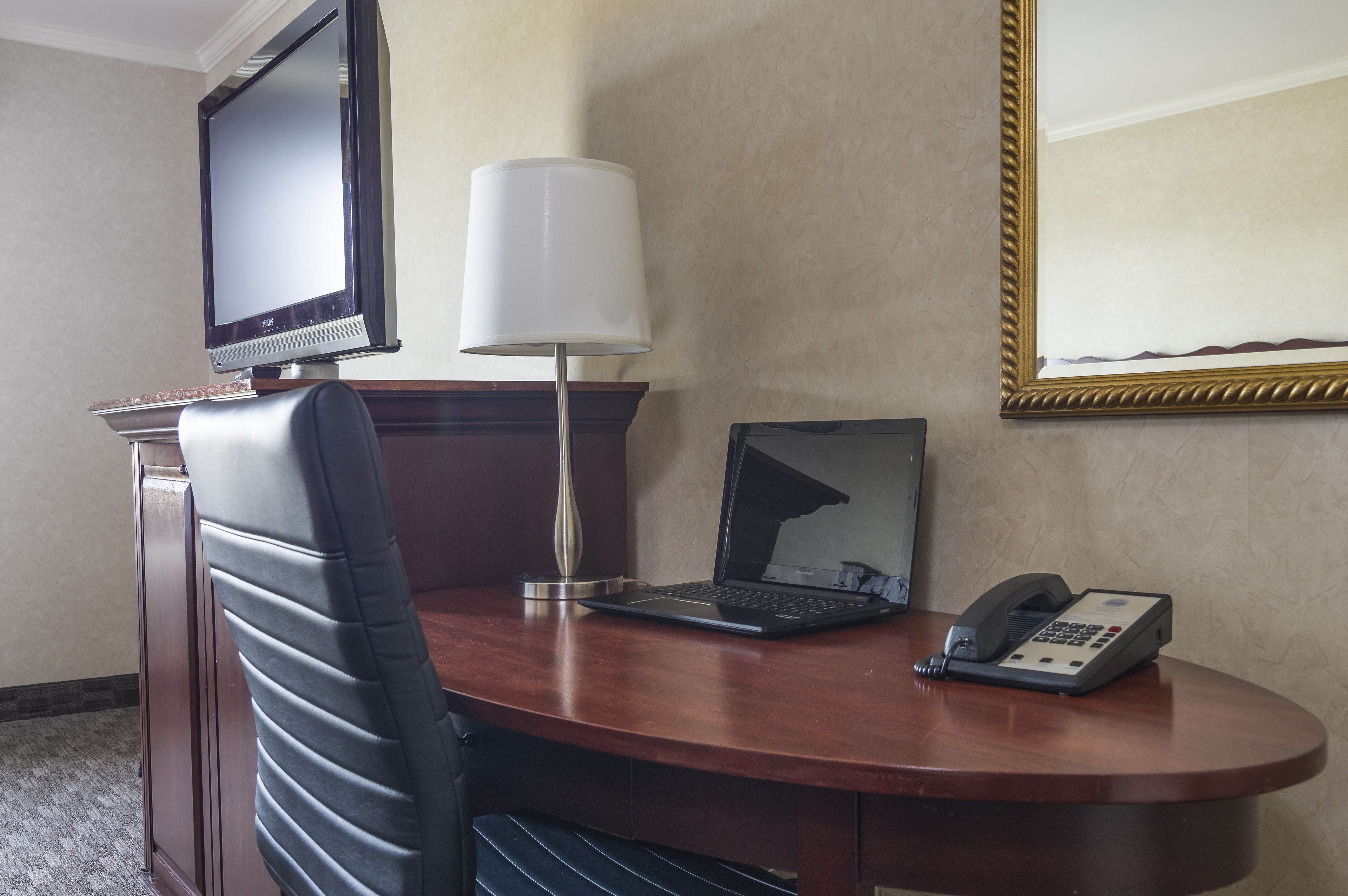 A hotel room with a desk, a laptop, a telephone, a television, and a lamp.