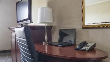 A hotel room with a desk, a laptop, a telephone, a television, and a lamp.