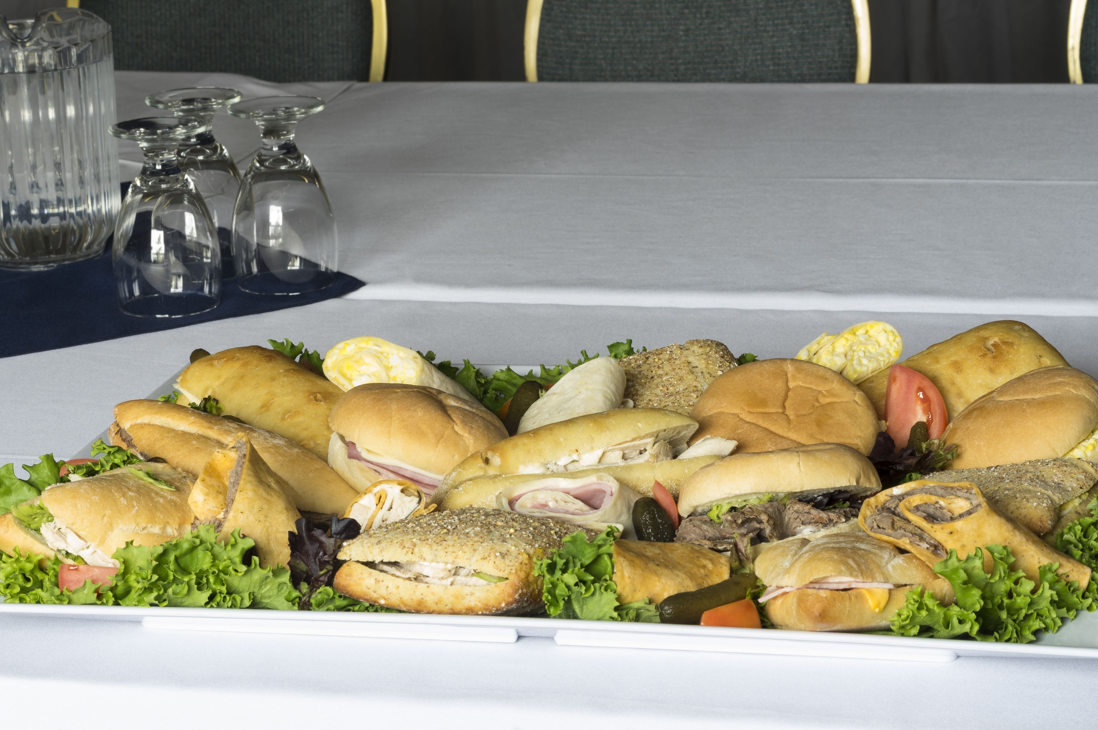 Una bandeja con varios sándwiches y ensaladas sobre una mesa con mantel blanco y saleros y pimenteros al fondo.