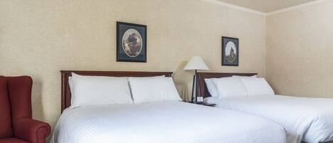 Habitación de hotel con dos camas, un sillón rojo y dos cuadros en la pared.