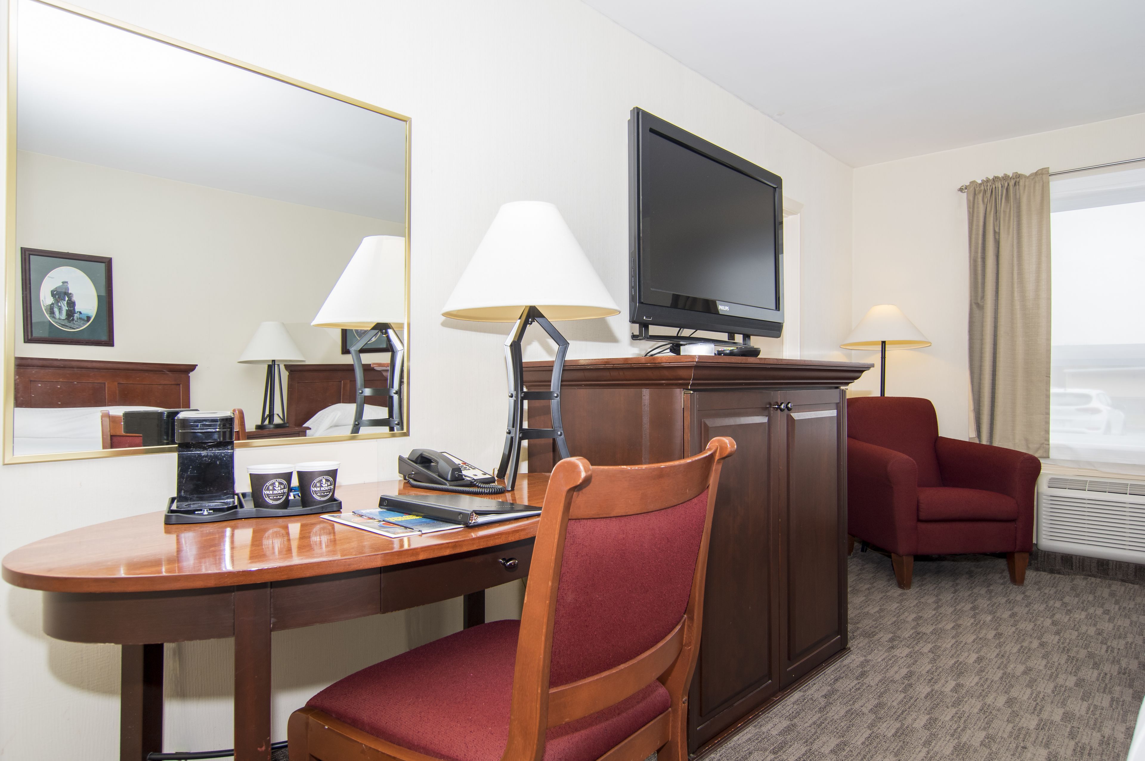 A hotel room with a desk, chair, television, and two lamps.