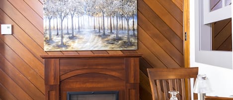 A wooden wall with a fireplace, a painting of trees, and a table with chairs.