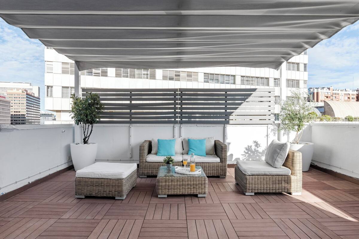 A rooftop terrace with wicker furniture, a covered seating area, and potted plants.