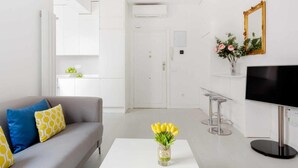 Un saló modern amb un sofà gris, una taula de centre blanca i una televisió. Hi ha una porta al fons i un ram de flors sobre la taula de centre.