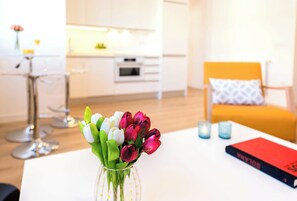 Ein modernes Wohnzimmer mit einem weißen Couchtisch, einer Tulpenvase, einem roten Buch und einem gelben Sessel.