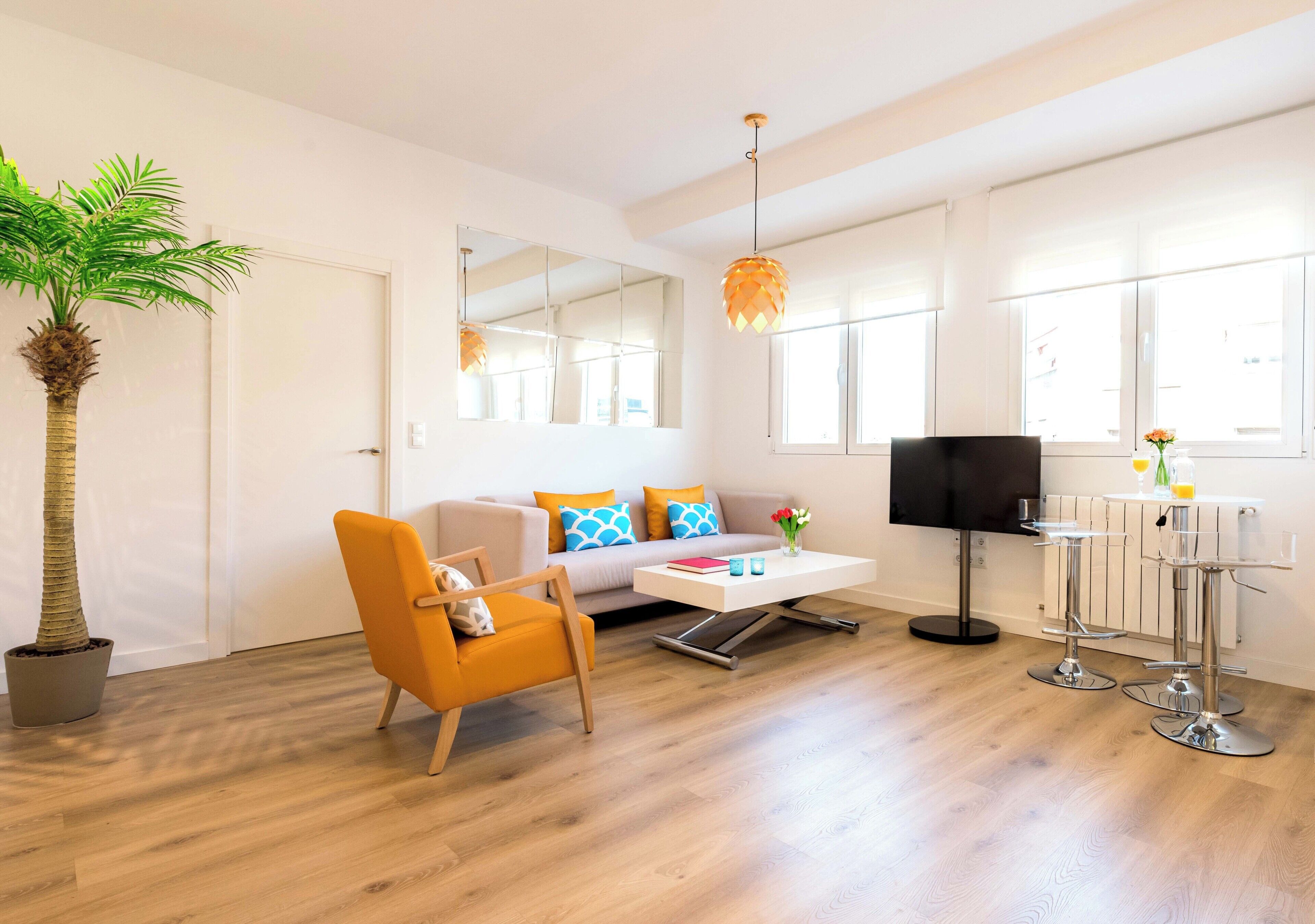 A modern living room with a sofa, armchair, coffee table, and a dining area with bar stools.