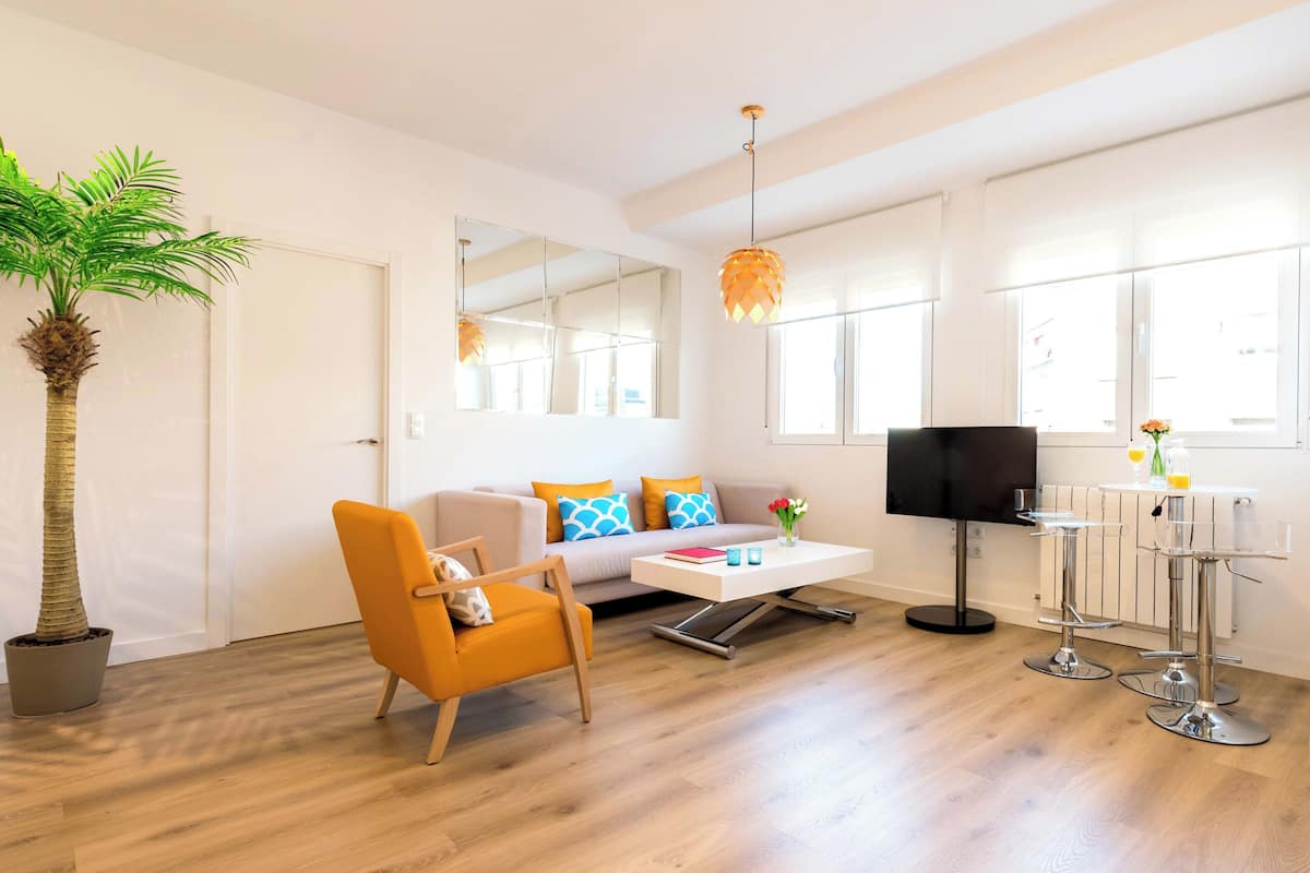 A modern living room with a sofa, armchair, coffee table, and a dining area with bar stools.