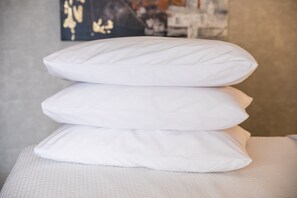 Almohadas blancas apiladas sobre una cama con una colcha blanca texturizada.