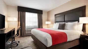 Une chambre d’hôtel avec un grand lit, un bureau, une chaise, une télévision et une fenêtre avec des rideaux.
