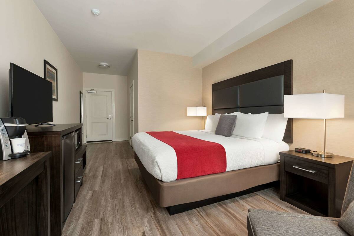 Une chambre d’hôtel équipée d’un lit, d’une table de chevet, d’une lampe, d’une télévision, d’une machine à café et d’un bureau avec une chaise.