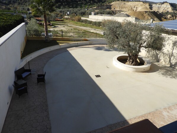 A curved outdoor patio with a seating area, a tree planter, and a view of a hilly landscape.