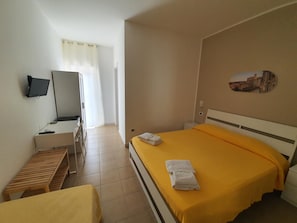 A hotel room with a bed, a desk, a chair, a TV, and a window with curtains.