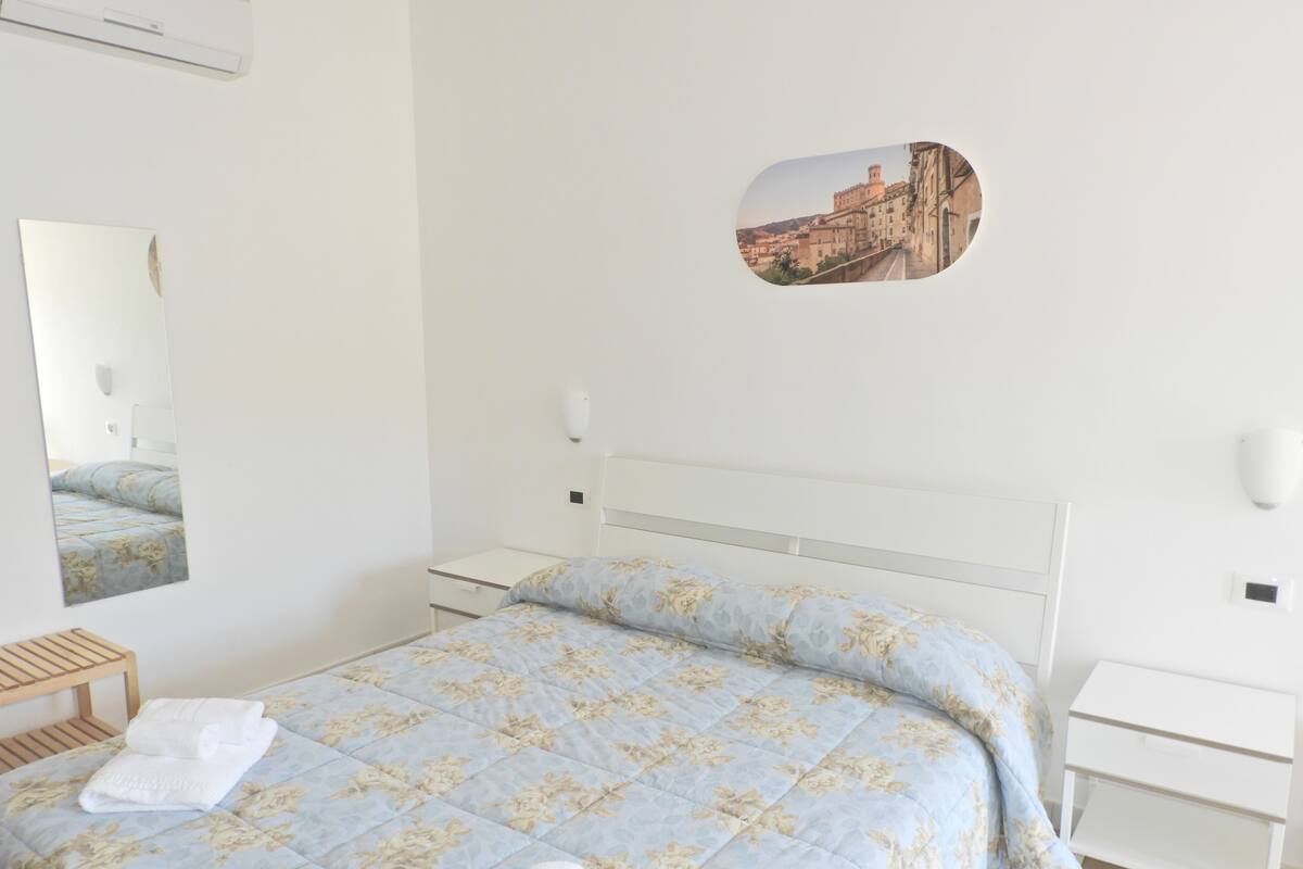 Une chambre à coucher avec un lit, une table de chevet, un miroir et un tableau accroché au mur.