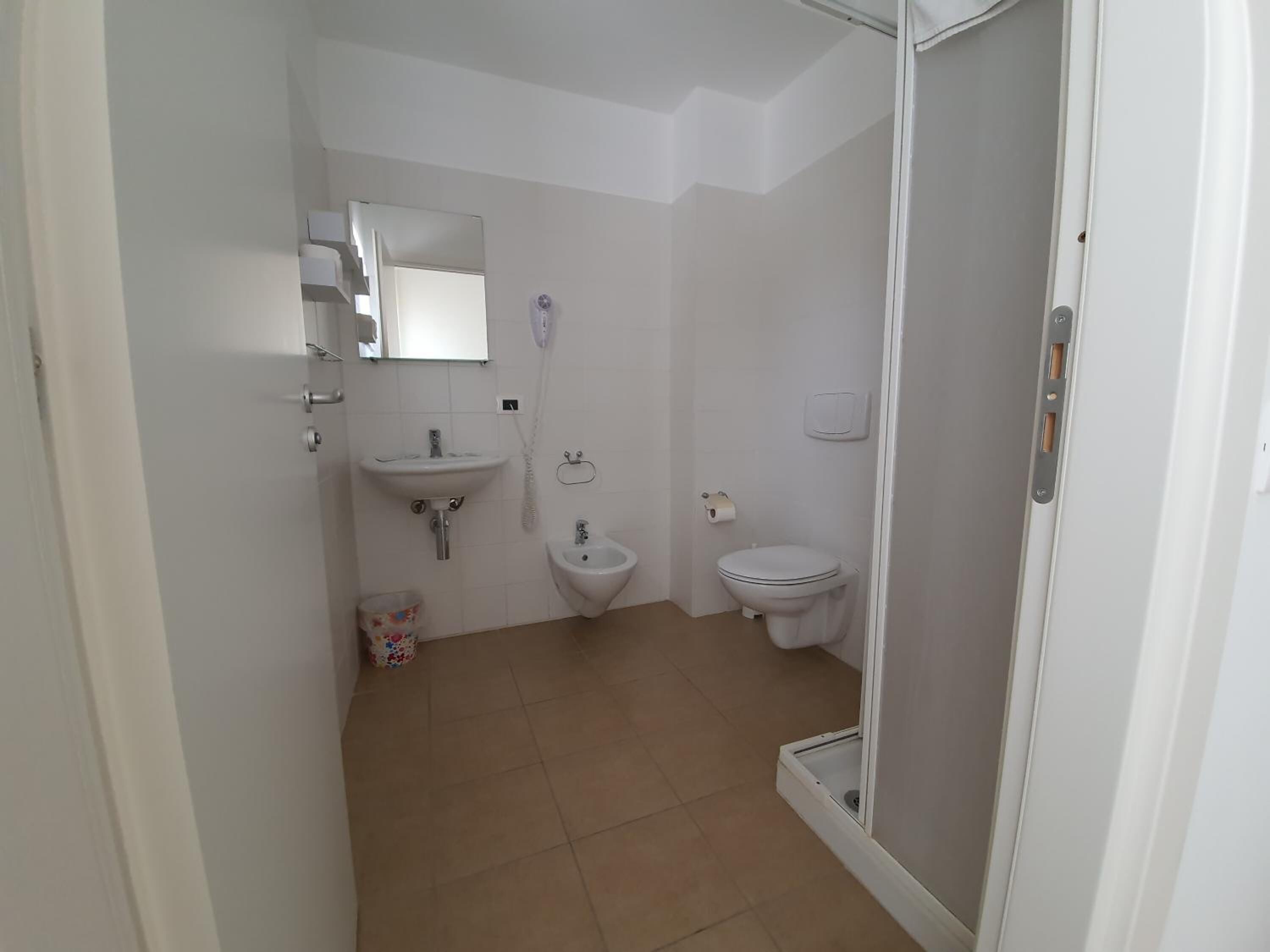 A small, clean bathroom with a toilet, bidet, sink, and a shower area.