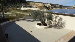 Un toit équipé de panneaux solaires, un jardinier circulaire avec un arbre, et une vue sur un paysage vallonné.