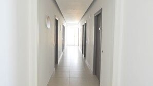 Un long couloir étroit aux murs blancs, avec des portes de chaque côté.