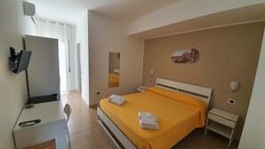 Une chambre d’hôtel avec un lit, un bureau, une chaise, une télévision, un miroir et un tableau au mur.