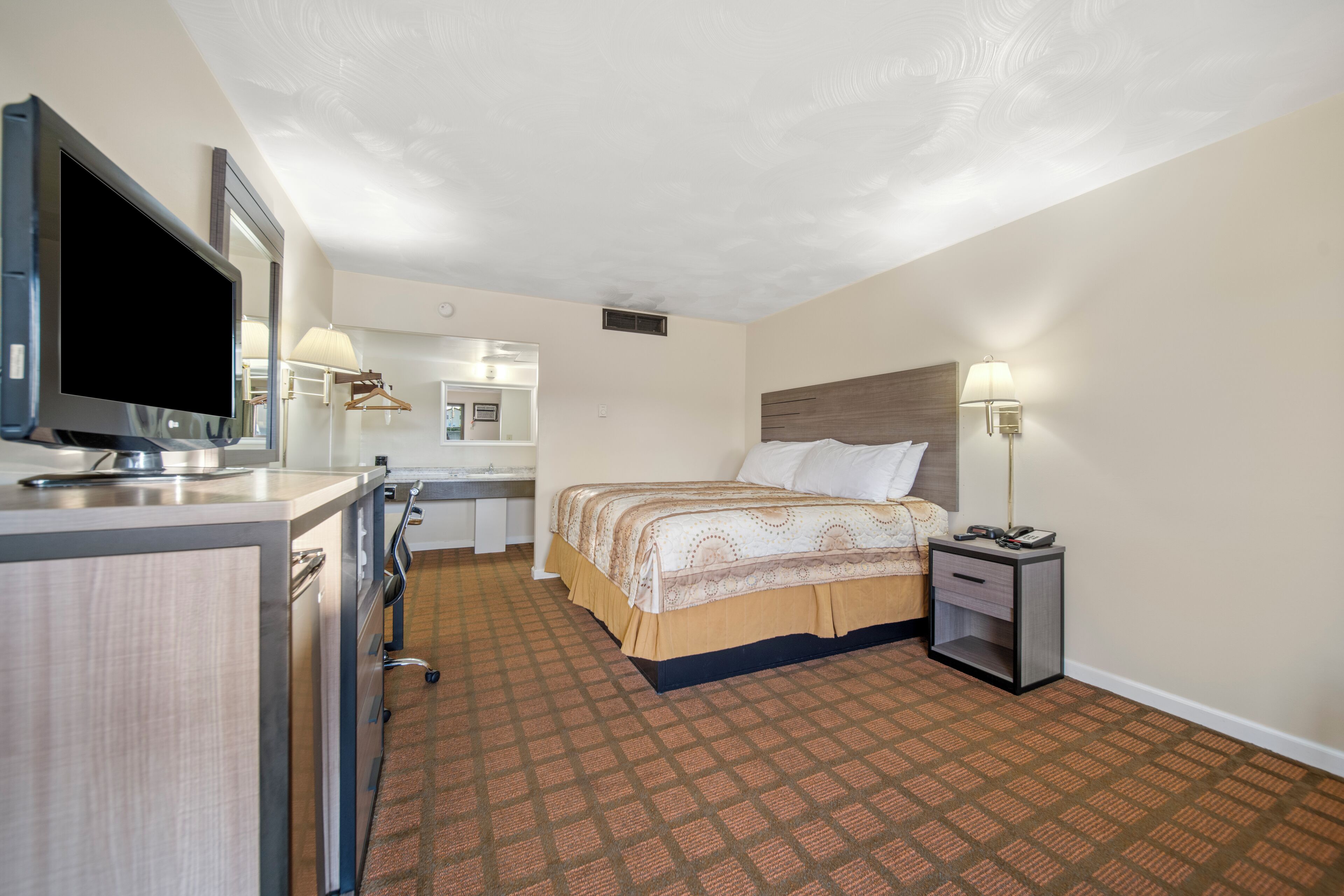 Une chambre d’hôtel avec un lit, une table de chevet, une lampe et un t éléviseur posé sur un bureau.