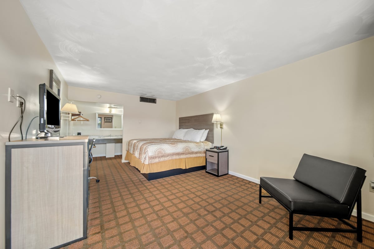 A hotel room with a bed, a desk, a chair, and a lamp.