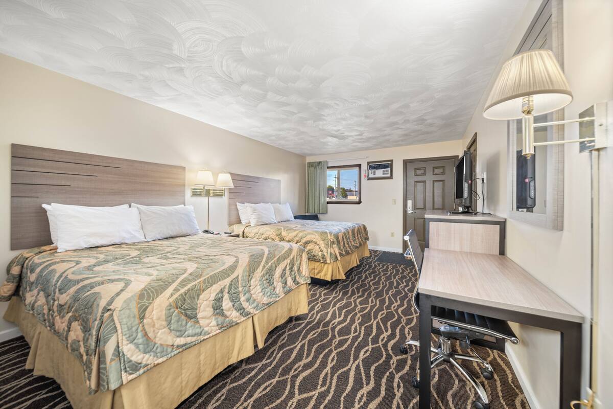 A hotel room with two beds, a desk, a chair, and a large window.