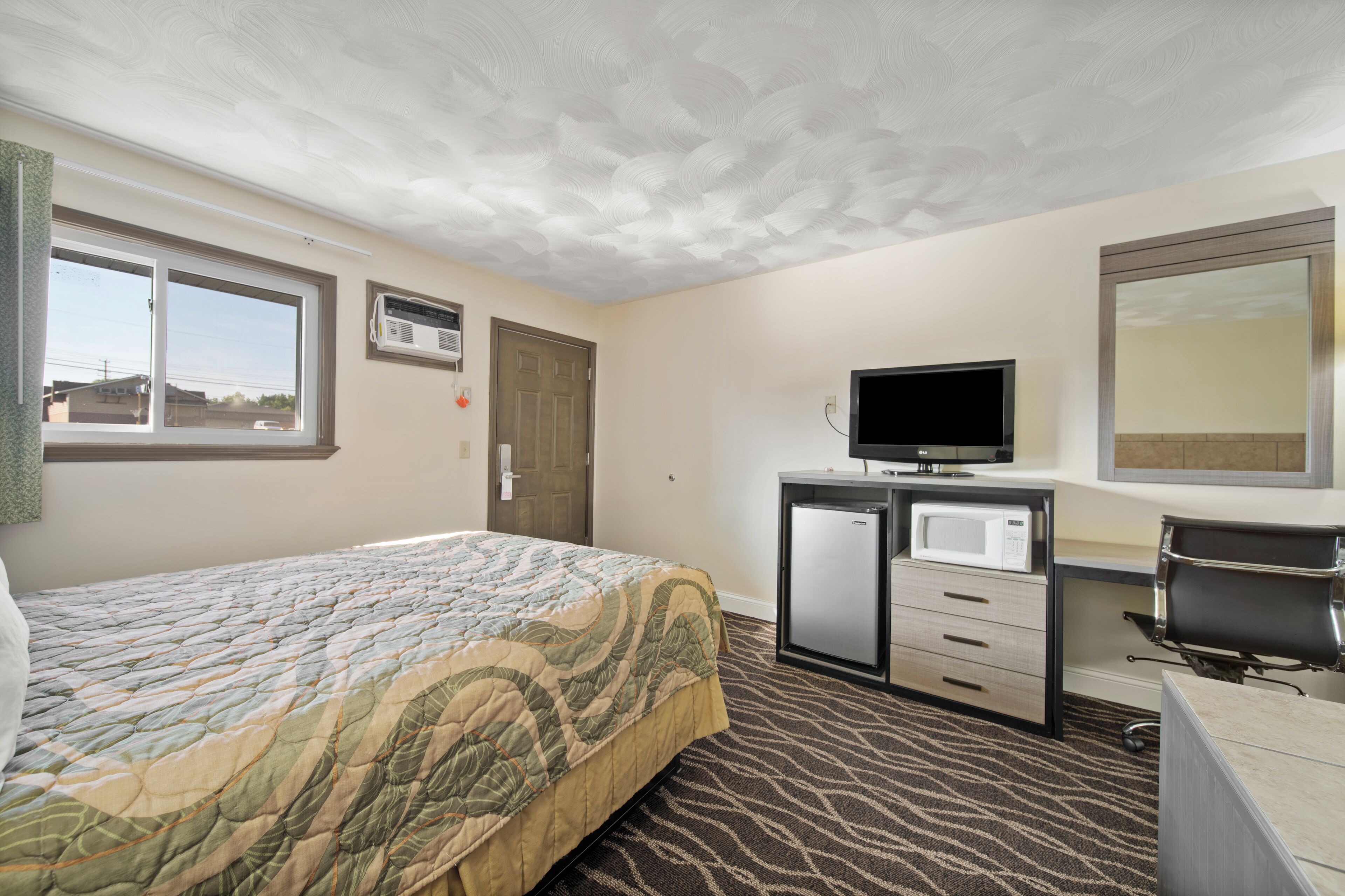 Une chambre d’hôtel comprenant un lit, un bureau avec une télévision, un four à micro-ondes et un miroir.