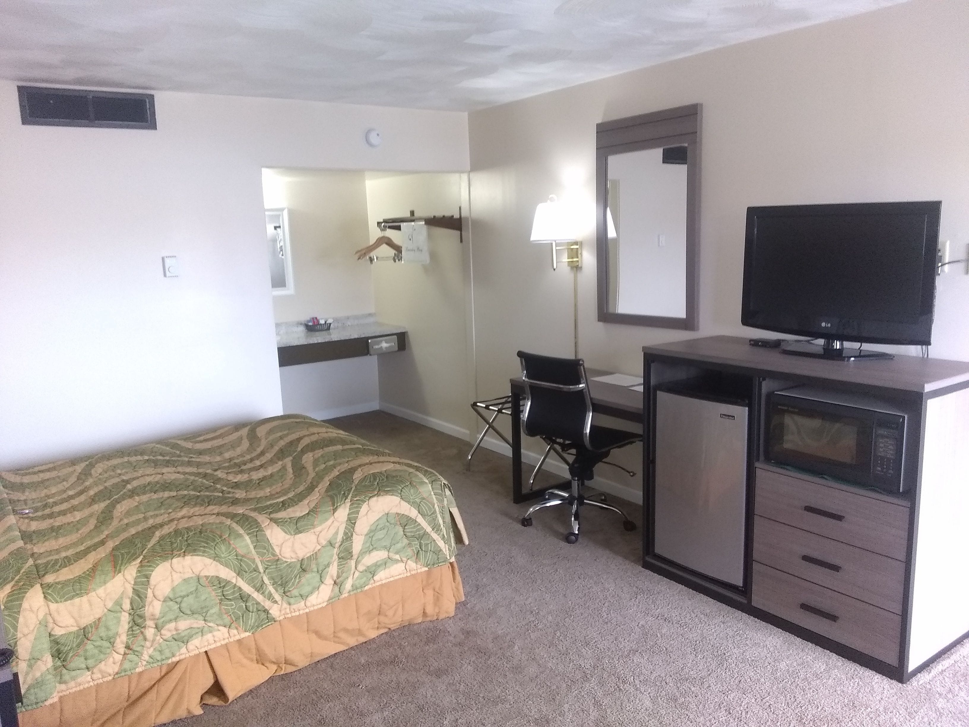 Una habitación de hotel con cama, escritorio, computadora, televisión y microondas.