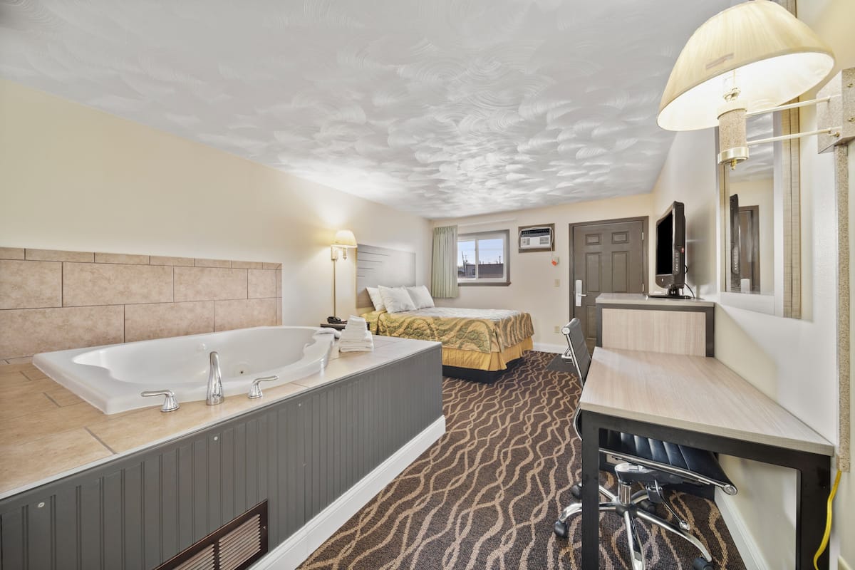 A hotel room with a large bathtub, a bed, a desk, and a television.
