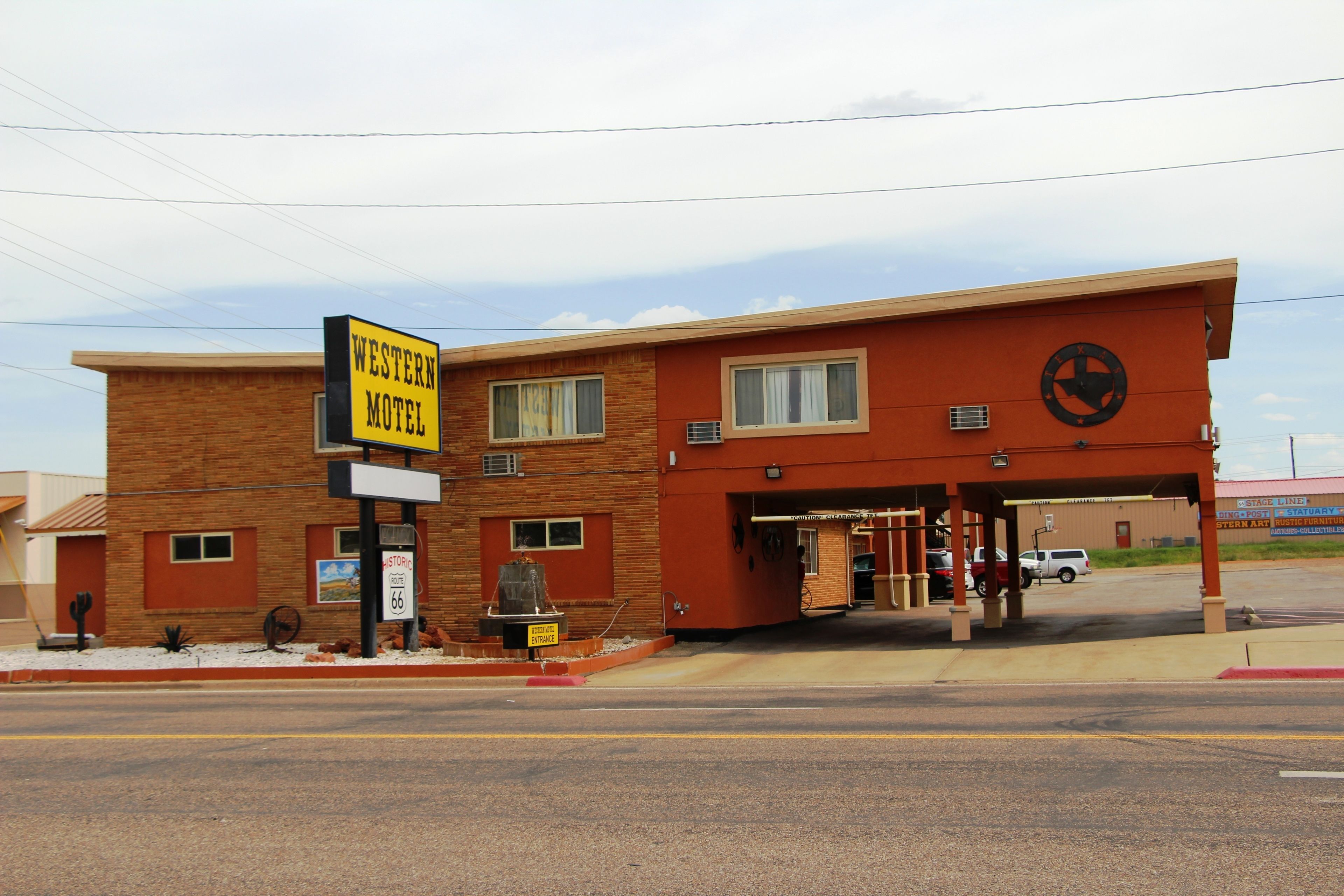 Un motel de style occidental, avec une façade en briques, un grand panneau indicateur et un espace de stationnement.