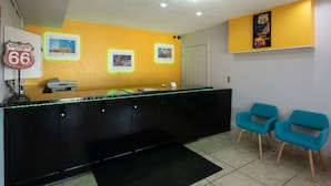 A reception desk with a black counter and neon lights, two blue chairs, and a wall with a 'Historic Route 66' sign. - Western Motel (Shamrock)