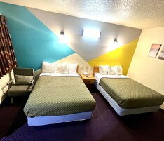Habitación de hotel con dos camas, una silla, una mesita de noche y una pared con un diseño geométrico.