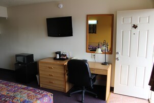 Habitación de hotel con cama, escritorio, silla, televisión, espejo y puerta.